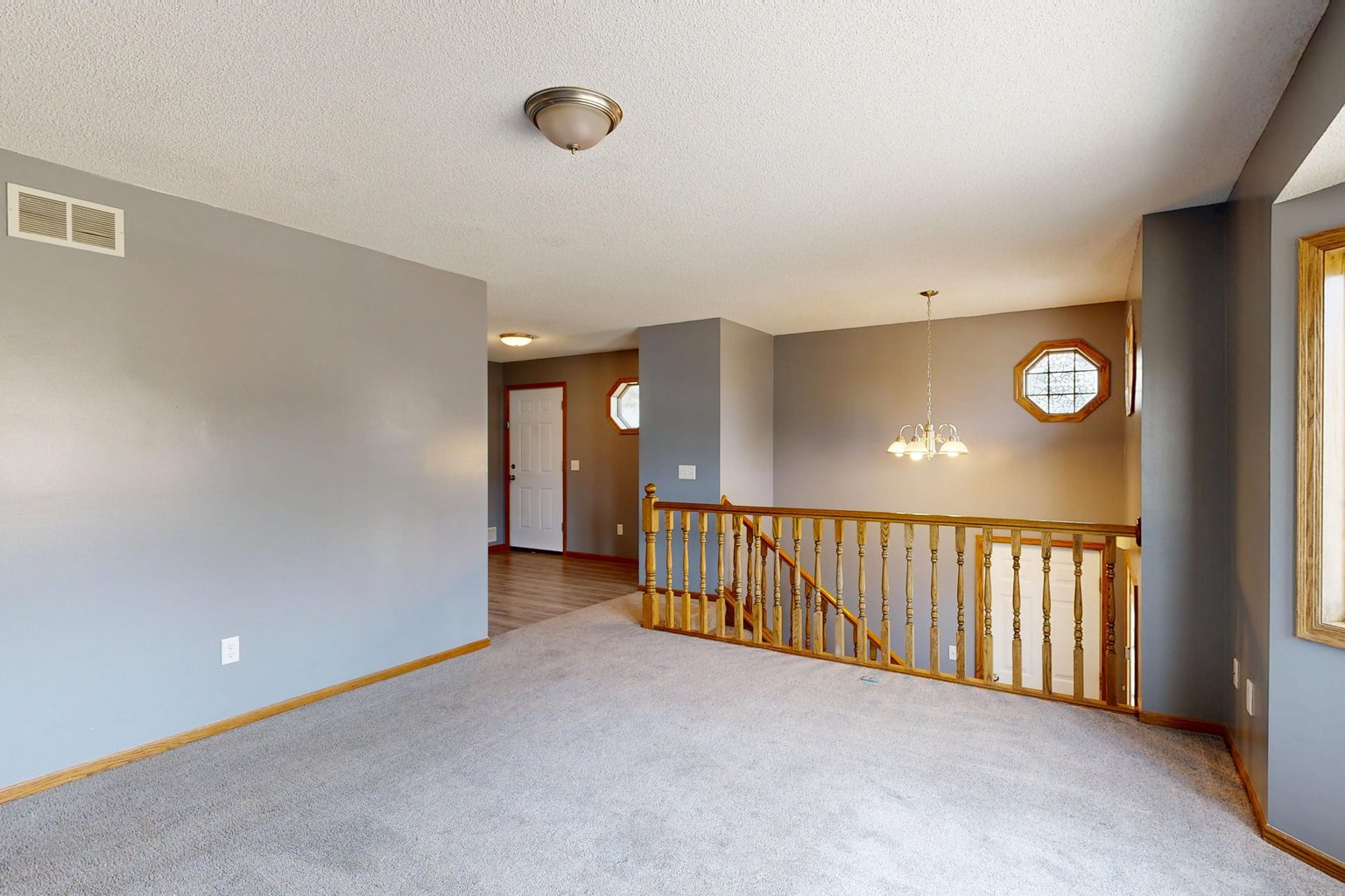 Residential room with gray wall-to-wall carpet, windows and a stair railing