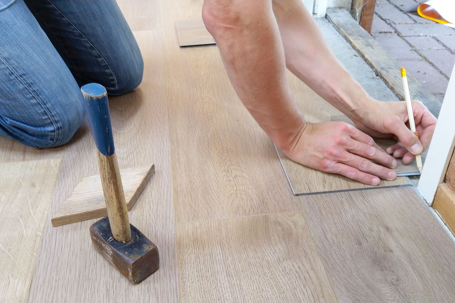 Installer measuring and marking a wood-look floor plank beside a door frame