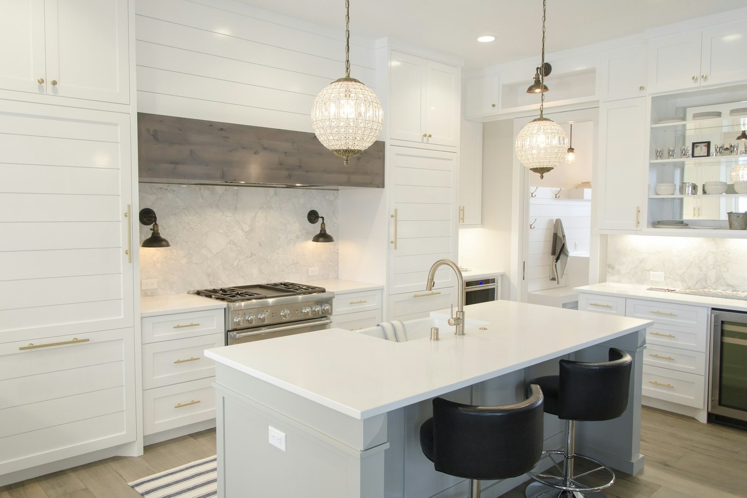 White residential kitchen with a large island, paneled cabinets and pendant lighting