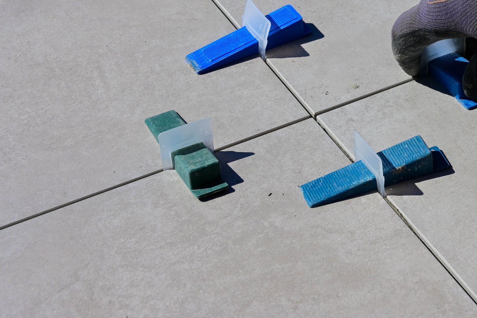 Gray floor tiles aligned with blue spacers during installation