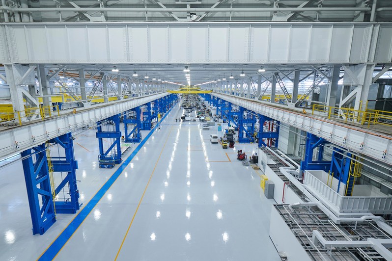 Reflective light floor and blue production fixtures inside an aircraft manufacturing facility.