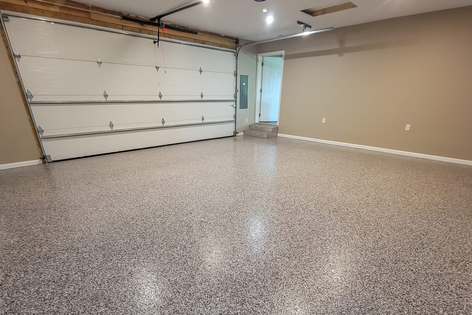 Residential garage with a completed decorative flake floor, beige walls, and a white overhead door.