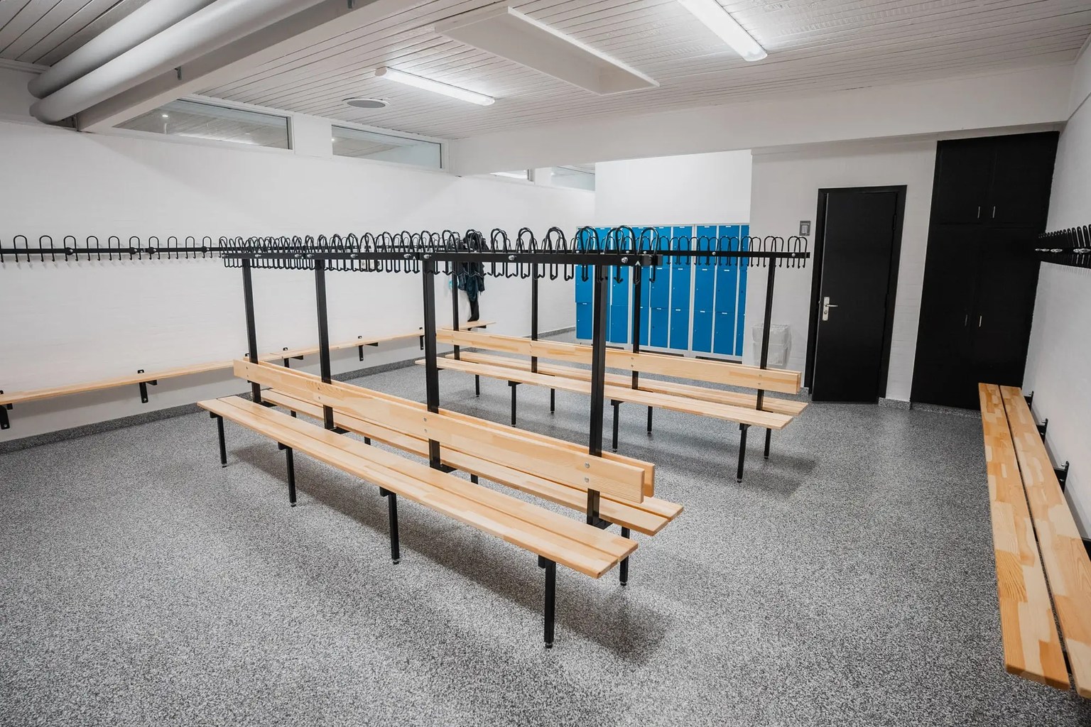 Locker room with blue lockers, wooden benches, black coat hooks, and a gray flake epoxy floor.