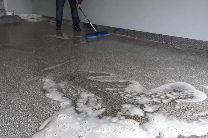 A person scrubbing a wet decorative flake floor with a long-handled blue brush.