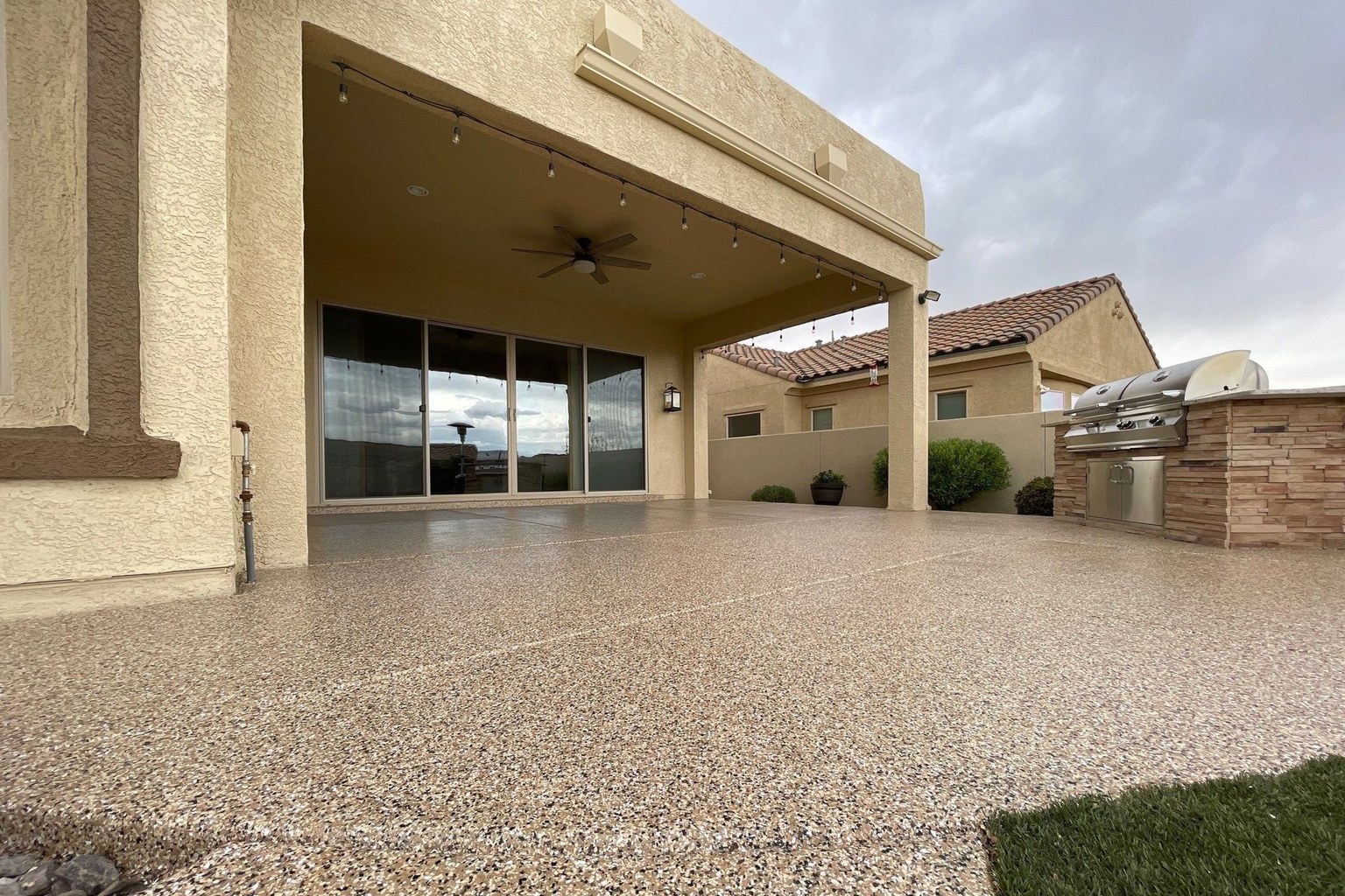 Outdoor concrete patio with a tan decorative flake coating beside a covered seating area and built-in grill.